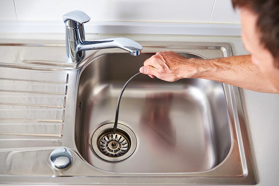 A drain snake being used to unblock a kitchen sink.