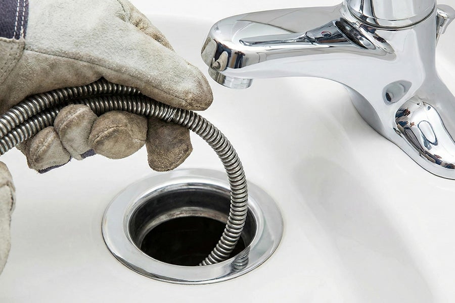 A drain snake being used to unclog a bathroom sink.
