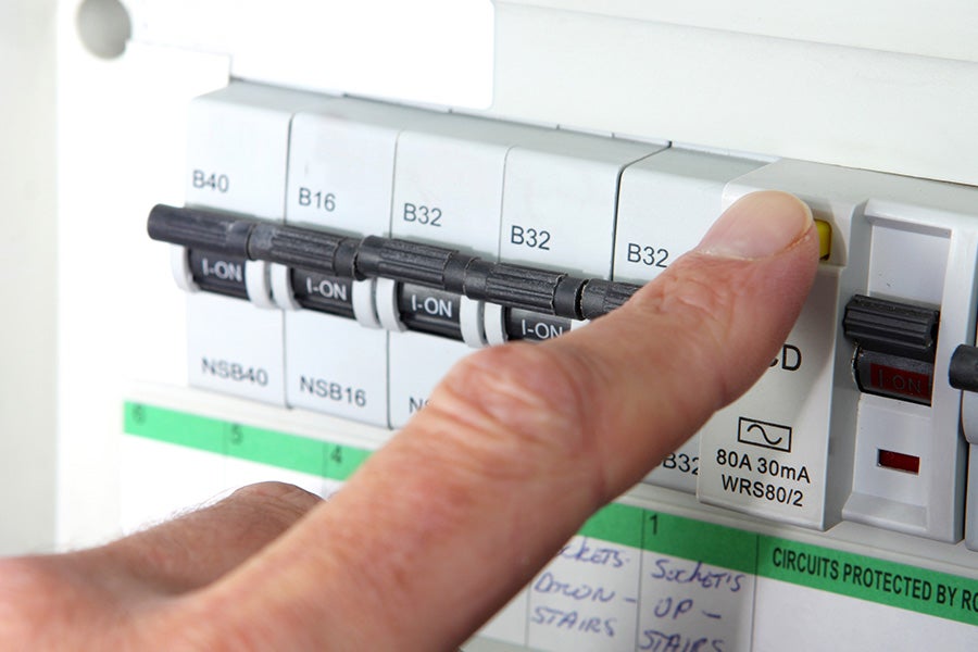 A modern fuse box (consumer unit) with someone pressing the RCD reset button.
