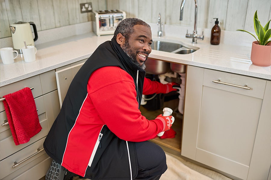 A HomeServe plumber fixing a leak under a kitchen sink.