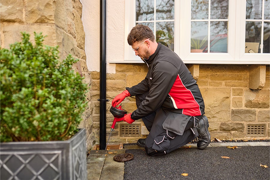 A HomeServe plumber unblocking an outside drain using a drain snake.