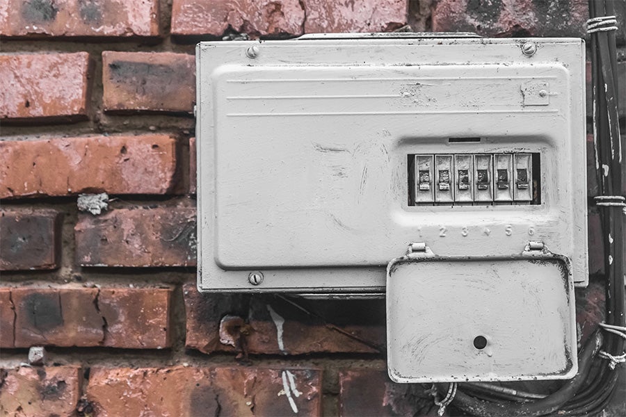 An older, damaged fuse box attached to a brick wall.
