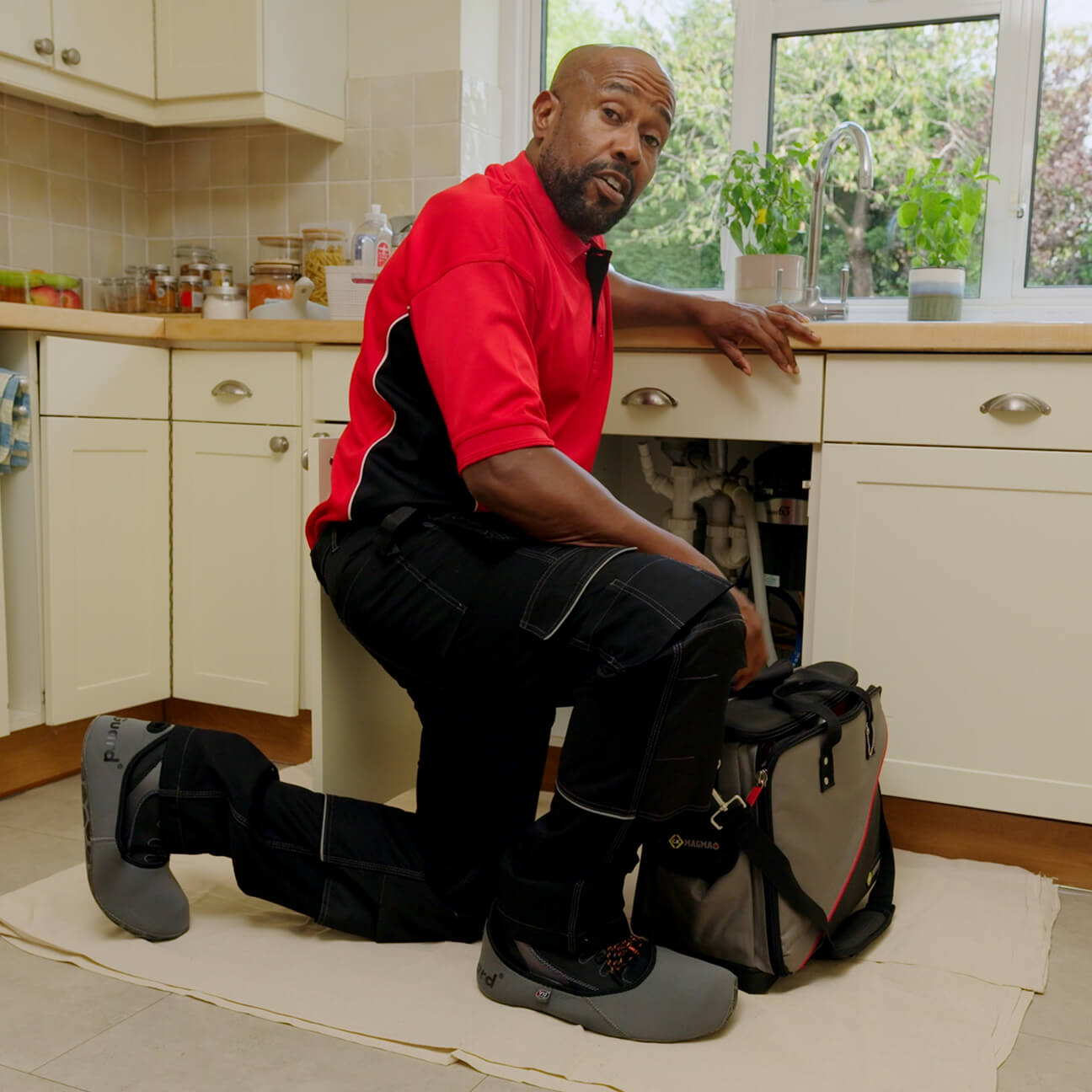 A HomeServe plumber fixing a plumbing problem under a customer's kitchen sink.