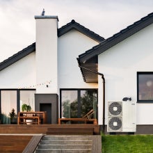  Heat Pump unit installed on the exterior wall of a contemporary home with greenery and blue sky in the background.