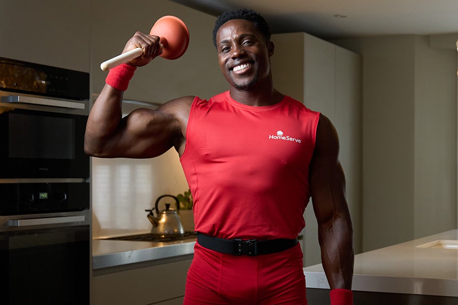 Harry Aikines-Aryeetey in a HomeServe uniform holding a plunger in a kitchen.