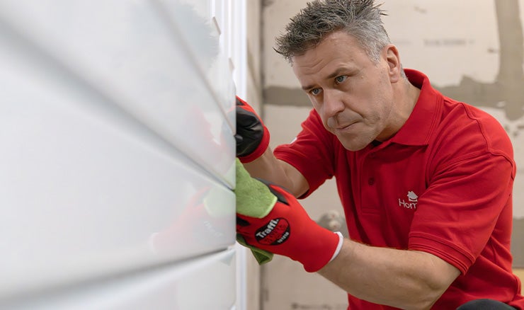 Craig Phillips crouches down to examine a radiator, wearing a red t-shirt.