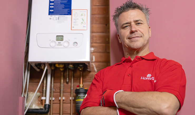 Craig Phillips stands in front of a white boiler wearing a red HomeServe t-shirt and gloves.