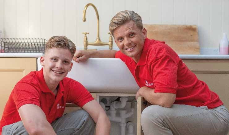 Jeff and Freddie Brazier crouching in front of a sink unit with the stopcock exposed.