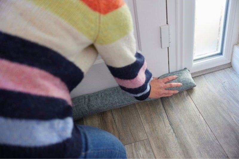 Woman in striped jumper draught proofing her front door