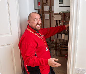 A HomeServe engineer checking pipes on a gas boiler while talking to a customer.