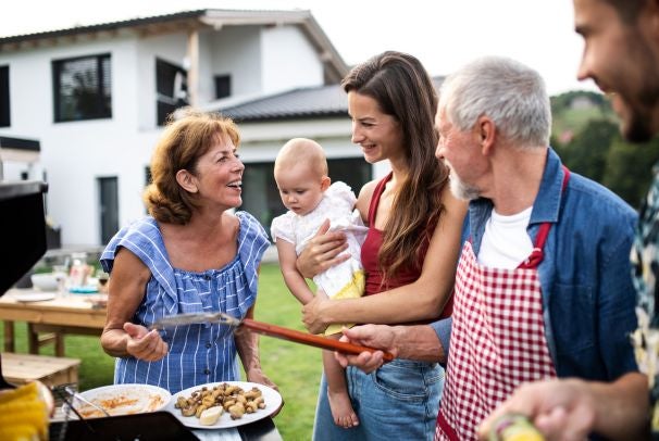 A family surrounding a BBQ in the garden with their home in the background