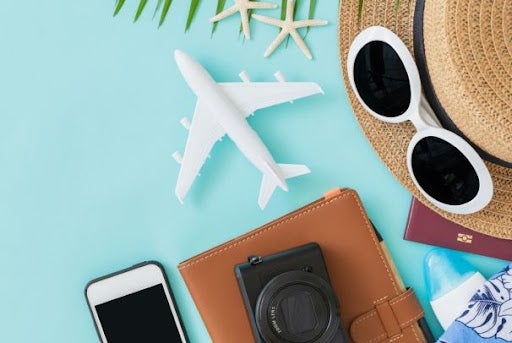 Summer essentials on a blue background, including a phone, passport, hat and camera